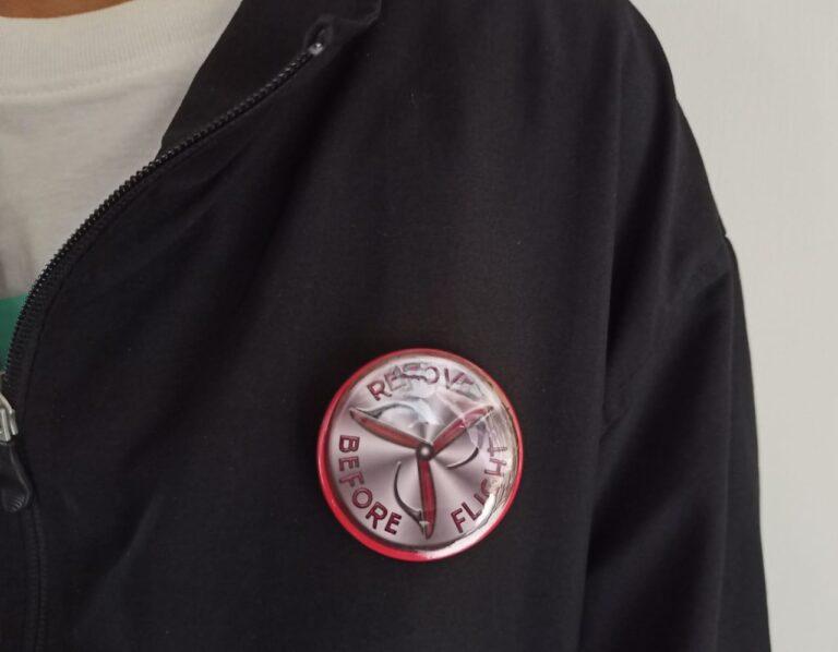 Image of Pin Badge 'Remove Before Flight' Silver Red Metallic with 3 Blade Prop on Jacket